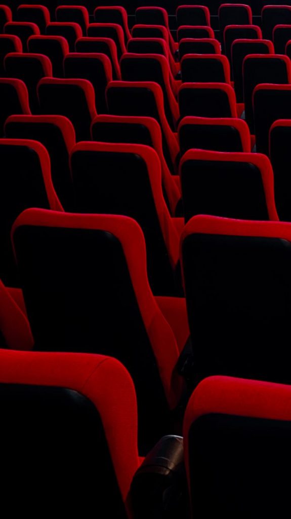 Rows of empty red theater seats in a dimly lit auditorium.
